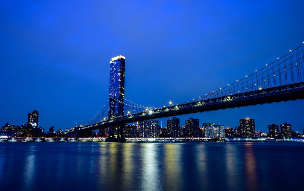 Stunning twilight view of a city skyline featuring a illuminated suspension bridge and river reflections.